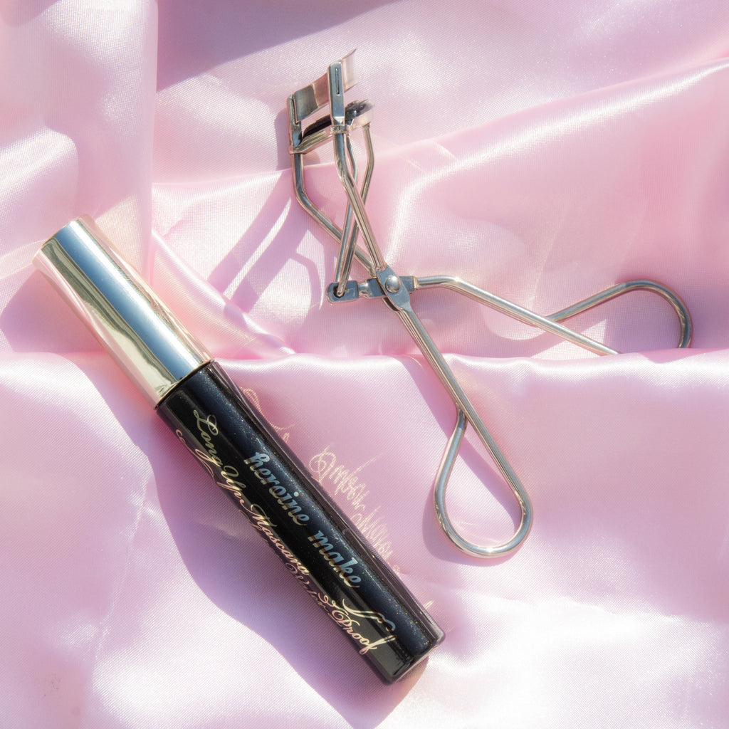 Heroine Make Kiss Me Long and Curl Mascara lying down on the ground with on pink background product review ヒロインメイク ロングUPマスカラ スーパーWP 01 ブラック