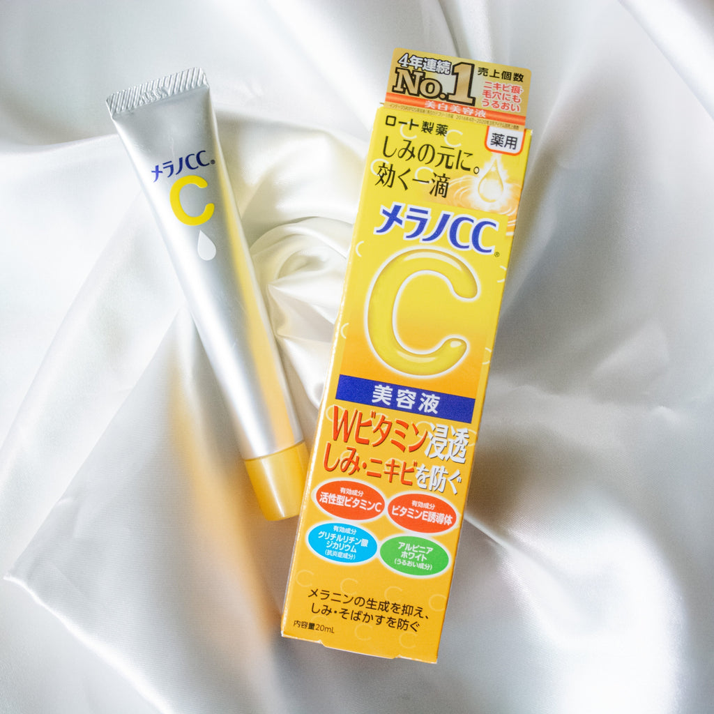 Melano CC Anti Spot Essence on silk backdrop, showcasing its bright yellow packaging and tube design.