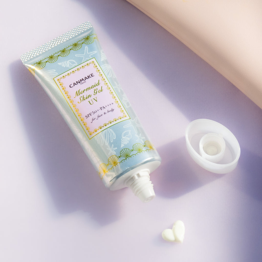 Canmake Mermaid Skin Gel UV sunscreen tube with SPF50+, lightweight gel, and heart-shaped cream on a pink background.