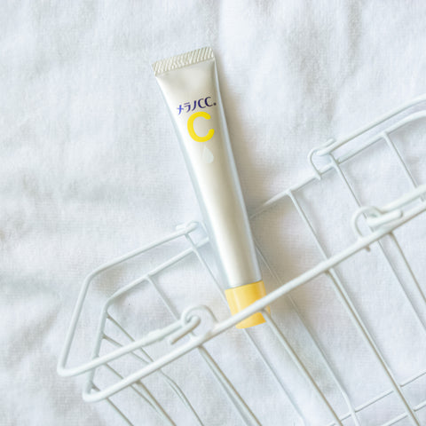 Melano CC Intensive Anti-Spot Essence tube resting in a wire basket against a soft white background